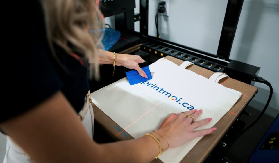 A printmoi.ca team member pressing the printmoi.ca logo onto a tote bag in the Edmundston shop